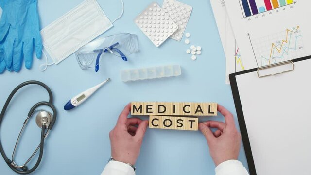 Phrase medical cost are made up of cubes on medical table by the hands of doctor, the view from above. Concept medicine financial costs.