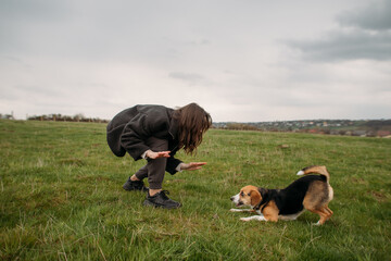young woman with a beagle dog running on a green field