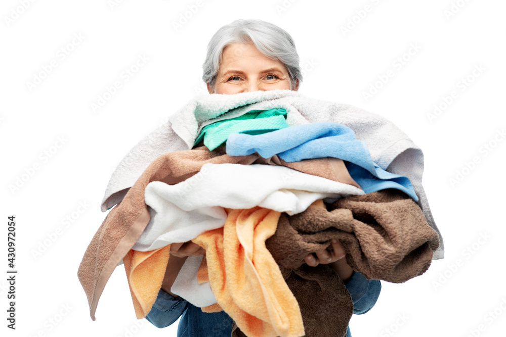 Poster cleaning, laundry and old people concept - senior woman in denim shirt with heap of bath towels over white background