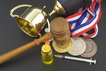 Broken golden winner cup with doping pills, syringe, medals and gavel as justice symbol on table,...