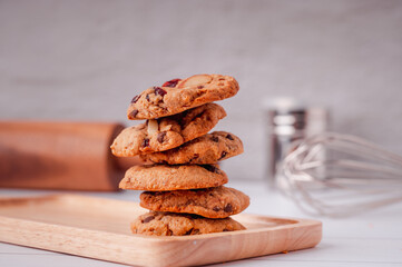 Piles of delicious chocolate chip cookies on a white plate with a milk bottle. Pastry utensils with white linen napkins on a wooden table. Delicious on a white plate with a bottle of milk.