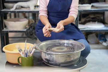 Cropped shot of woman in blue apron creating handmade clay ceramics in pottery workshop studio