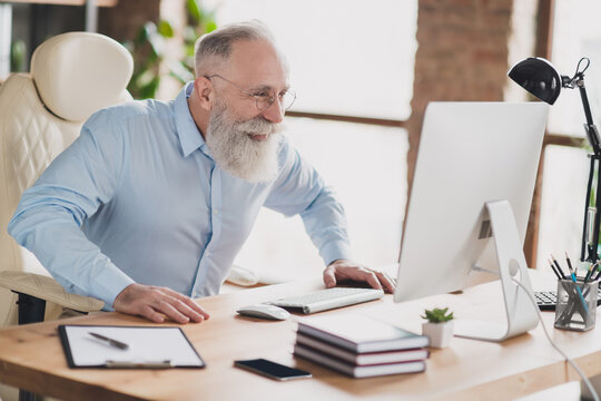 Photo of cheerful positive charming old businessman wear glasses look computer sit table indoors inside office
