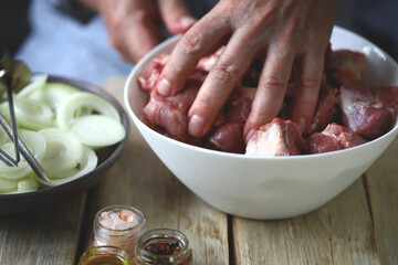 Pieces of raw meat for barbecue and onion rings in a bowl. Hands stir the marinated meat.