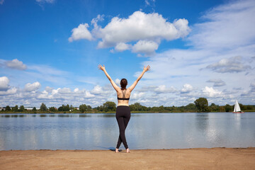 Fototapeta na wymiar Sporty attractive young woman wearing black trendy sportswear stretching near lake outdoor and do morning exercises.
