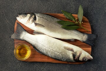 Fresh raw sea bass on a cutting board with olive oil and laurel leaf.