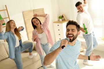 Fototapeta premium Young man singing karaoke with friends at home