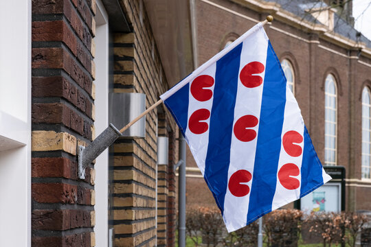 The tricolor Frisian flag, provincial flag of Friesland province, hangs from a flagpole against a wall in Koudum, the Netherlands. In the background the church