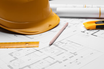 Pencil, ruler and hardhat on blueprints, closeup