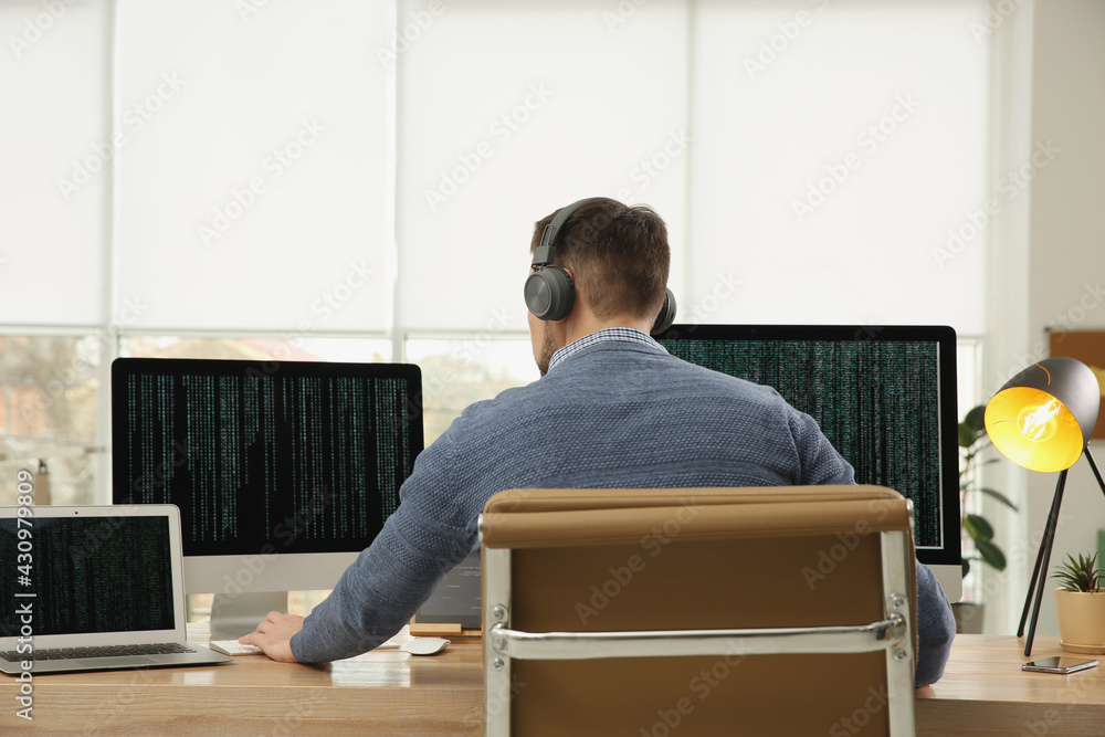 Poster programmer with headphones working at desk in office
