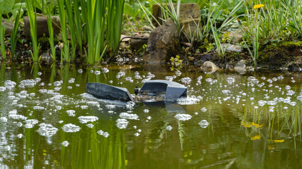 Skimmer Messner floats on surface of water in garden pond against blurred background of stone banks. Selective focus. Skimmer removes debris and dirt and saturates water with air.