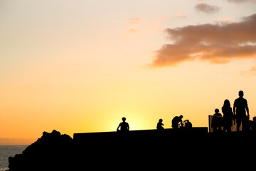 Fototapeta na wymiar silhouettes of caucasian man practicing yoga at sunset in sea promenade with people walking , Madeira island