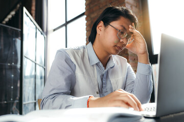 Tired asian businessman working at laptop and touching his head with his hand for headache