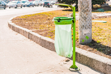 Light green garbage bag hanging on a metallic construction on the sidewalk. Trash bag. Rubbish can....