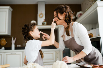 Mom and daughter in aprons fool around with each other soiling their noses with flour with their fingers