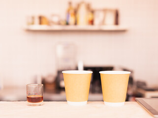 Two takeaway coffee cups and coffee measure cup are placing on coffee counter bar.