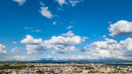 Image of a day with the blue sky and some white clouds. At the base of the image is a city and mountains in the background. 
