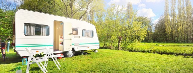 White caravan trailer on a green lawn in a camping site. Sunny day. Spring landscape. Europe. Lifestyle, travel, ecotourism, road trip, journey, vacations, recreation, transportation, RV, motorhome - obrazy, fototapety, plakaty