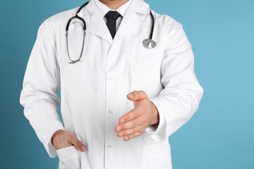 Doctor offering handshake on light blue background, closeup