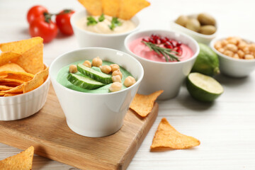 Different kinds of tasty hummus served with nachos on white wooden table, space for text