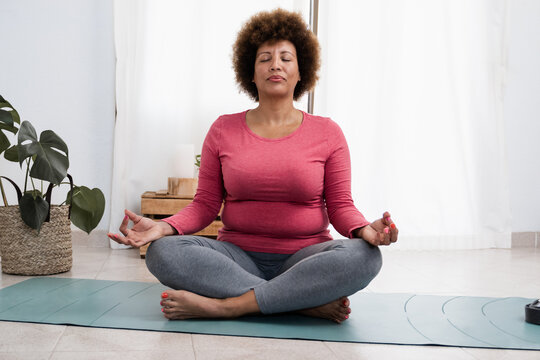 Curvy african senior woman doing pranayama breath exercises during yoga session at home - Focus on face
