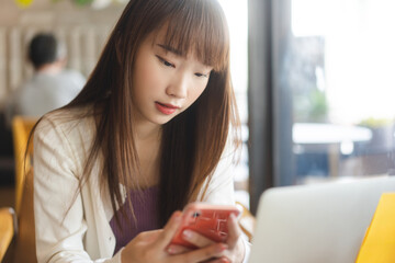 Young adult asian student woman using mobile phone for online application at indoor cafe.