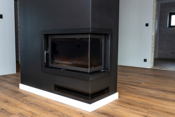 A modern standing fireplace in the living room enclosed with panels, painted black with a corner pane covered with soot.