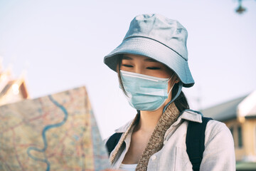 Adult traveller asian woman wear face mask for protect virus corona or covid 19 using map for searching destination.