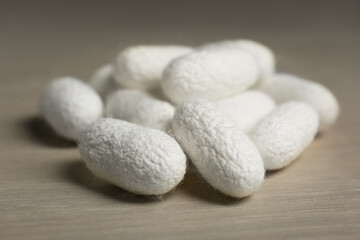 Heap of white silk cocoons on wooden table, closeup