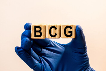 The word BCG which is made from wooden cubes. Hands in a blue glove. Isolated on WHITE background