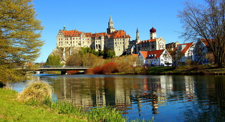 herrliches Schloss Sigmaringen spiegelt sich unter blauem Himmel vor grünen Ufer der Donau 