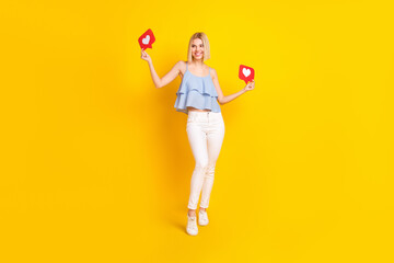 Full length photo of cheerful blond hair lady hold likes look empty space wear top pants isolated on yellow background