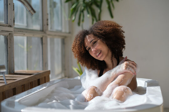 Smiling and relaxing african american woman bathing in a tub full of foam. Amazing time. lifestyle people concept - Powered by Adobe