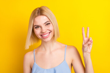 Photo of optimistic blond short hair lady show v-sign wear blue top isolated on yellow color background