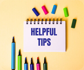 The words HELPFUL TIPS written in a white notebook on a beige background near multi-colored markers