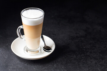 latte macchiato in a glass with a handle and on a white plate and spoon on a black background, space for text