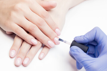 Concept process manicure. Manicurist uses brush to apply pink gel polish to woman client nail