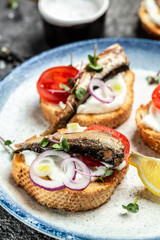 Fototapeta na wymiar Sandwiches with sprats on toasted bread with fish, fresh tomatoes and onion. Food recipe background. Close up