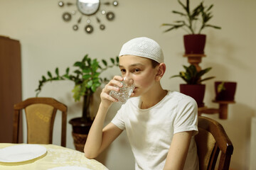 a boy in an Islamic costume drinks water during Iftar in the month of Ramadan.