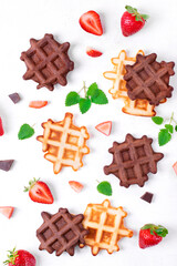Two types of waffles with strawberry and mint on white table. Classic and chocolate variation of the dessert. Flat lay
