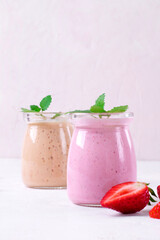 Pink and yellow smoothies topped with mint in glass jars on the white table. Healthy drink and kids food