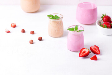 Pink and yellow smoothies topped with mint in glass jars on the white table. Healthy drink and kids food