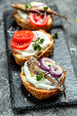 Sandwich with sprats, tomatoes and onion with microgreen on a slate board, top view