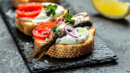 Sandwich with sprats, tomatoes, onion and microgreen on a slate board, Danish cuisine. Food recipe background. Close up