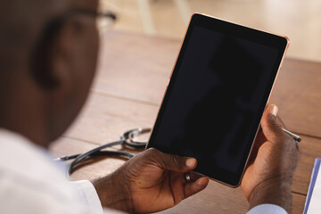 Mid section of african american senior male doctor holding digital tablet with copy space at home