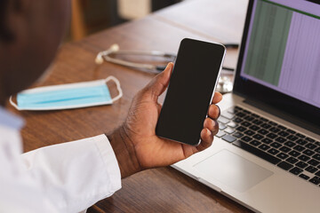 Mid section of african american senior male doctor holding smartphone with copy space at home