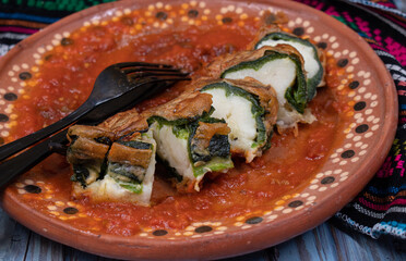 Mexican sliced vegetarian chile rellenos filled with potato and cheese, on mole, in traditional clay plates