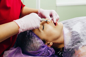 Obraz na płótnie Canvas Woman gets an injection with hyaluronic acid as a dermal filler for lip enlargement