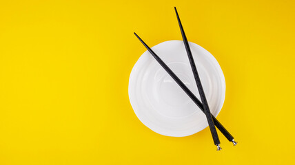black chopsticks for sushi in a white saucer on a yellow background, isolated