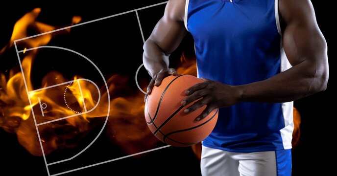 Composition of midsection of basketball player holding basketball over basketball court and fire
